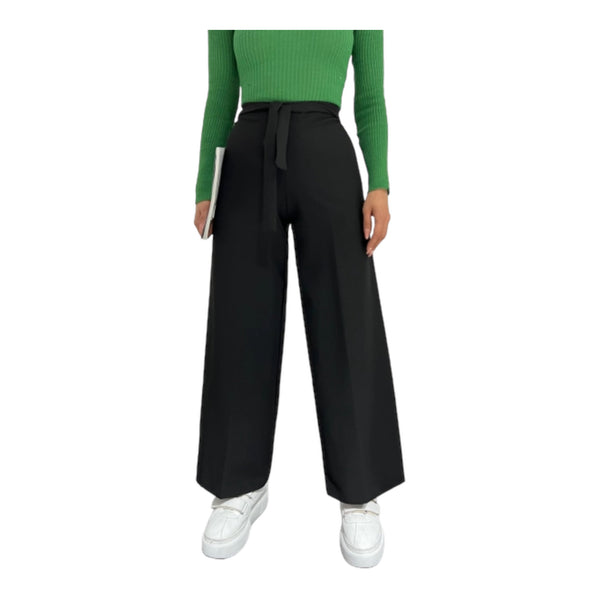 Woman wearing mid-rise wide-leg trousers in black, with an elastic waistband, paired with a green top and white shoes.