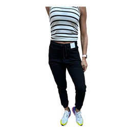 A pair of black long joggers with an elastic waistband, double zipper side pockets, and a slim fit. The joggers are modeled by a person wearing a striped crop top and white sneakers.