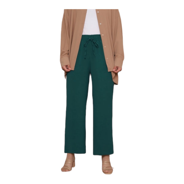 A woman standing, wearing emerald green wide leg pants with an elastic waistband and drawstrings, paired with a beige cardigan and white top.