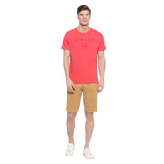 Full body view of model in pink GANT logo shield T-shirt styled with tan shorts and sneakers