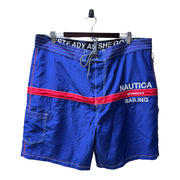 Men's navy blue swim boardshorts with red accents and Nautica branding on the side, displayed on a hanger.