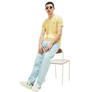 Man sitting on chair wearing Lacoste yellow V-neck T-shirt with small green crocodile logo and light wash jeans