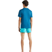 Back view of Vilebrequin blue polo shirt worn by model with turquoise turtle print swim shorts